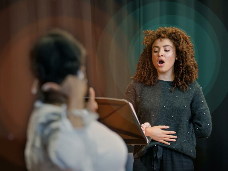 Person holding their hand to their stomach singing, stood in front of a music stand