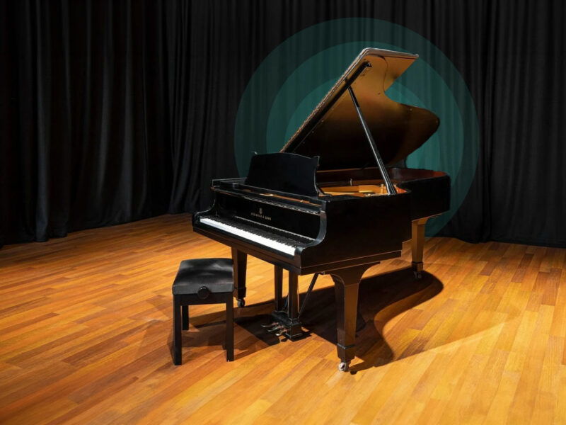 Grand piano in front of draping curtains, with spotlight on the top of the piano