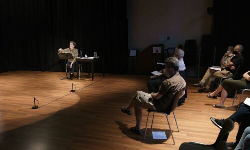 Masterclass from Dame Sarah Connolly - someone is stood on stage with someone just to the right. There is a group of people holding papers in the audience watching.