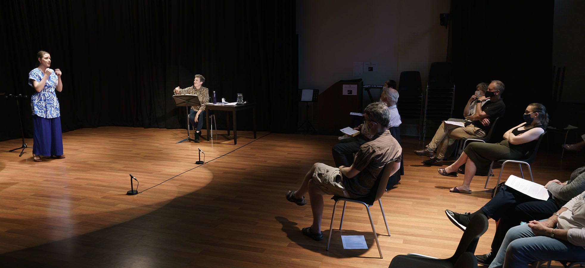 Masterclass from Dame Sarah Connolly - someone is stood on stage with someone just to the right. There is a group of people holding papers in the audience watching.