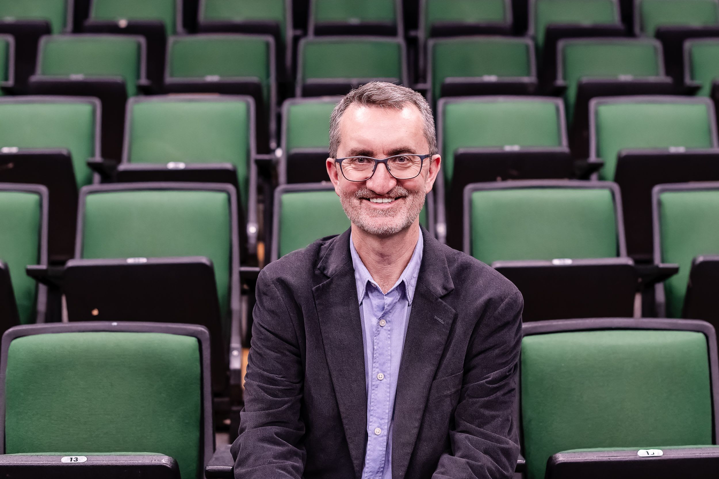 Person sat smiling on the front row of multiple rows of green chairs