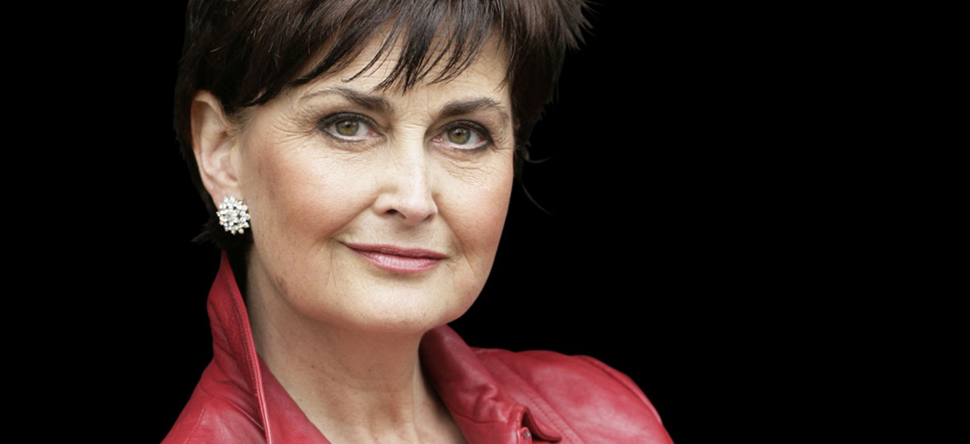 Portrait of Kathryn Harries. They are smiling at the camera wearing a red leather jacket.