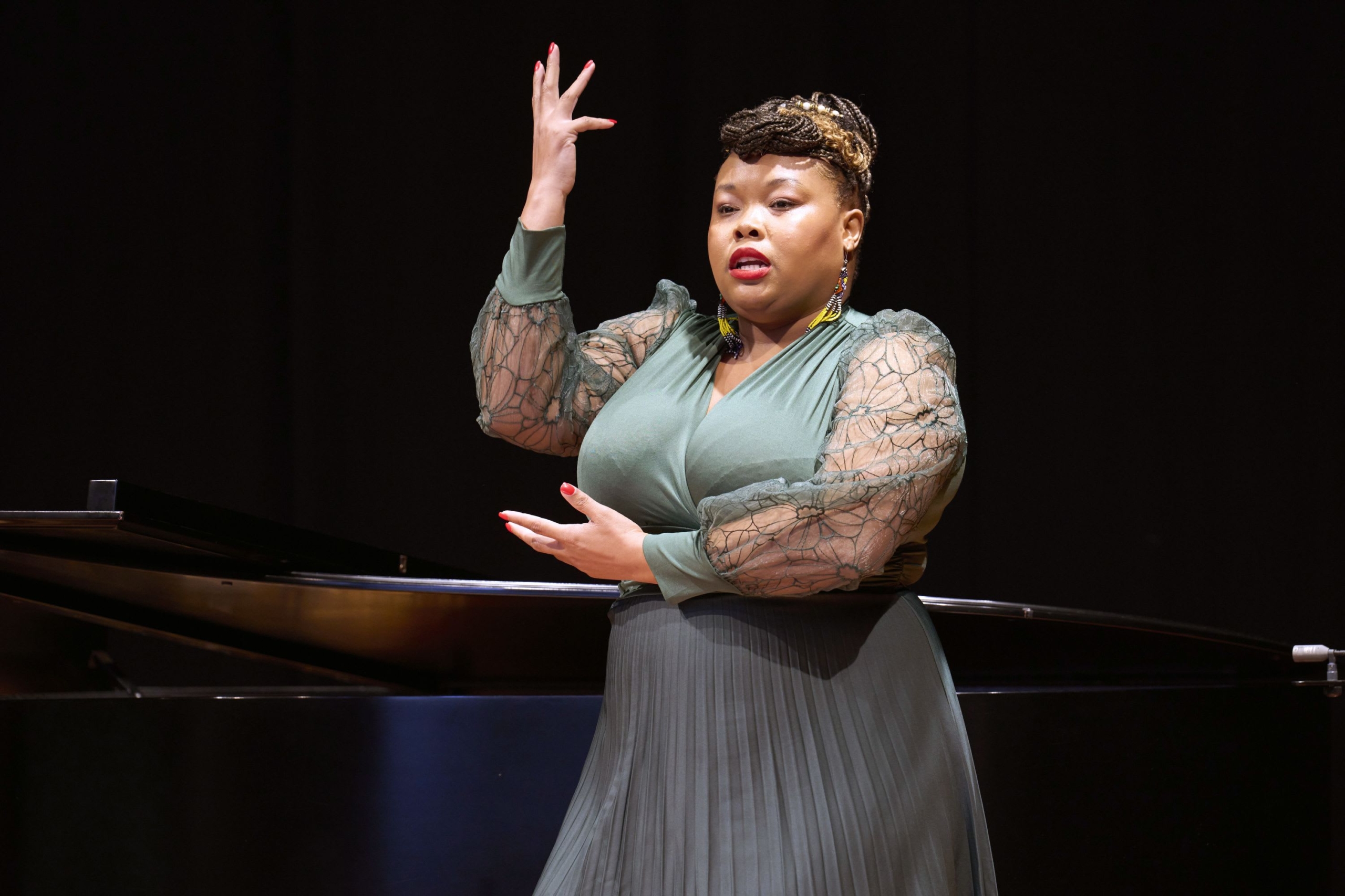 Person on stage holding one arm across the front of them and another arm up in the air