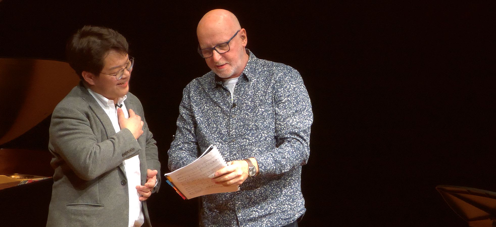 Two people on stage during a masterclass. The person on the right is showing the other person sheet music
