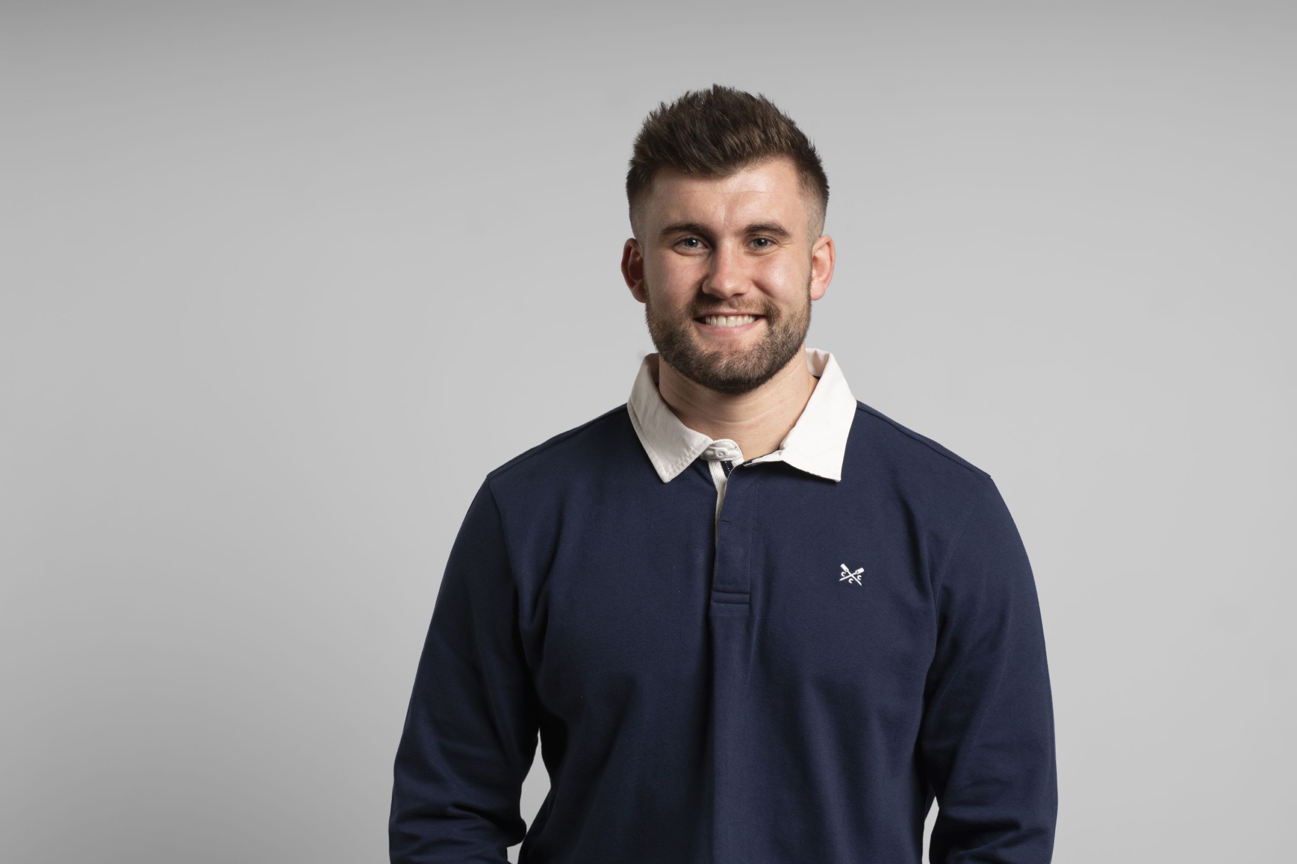Portrait of Rhydian Jenkins, they are wearing a long sleeve polo and are smiling.