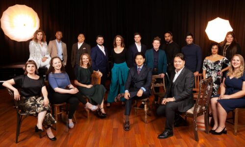 Group of young artists sat together, they are all wearing formal clothing and smiling.