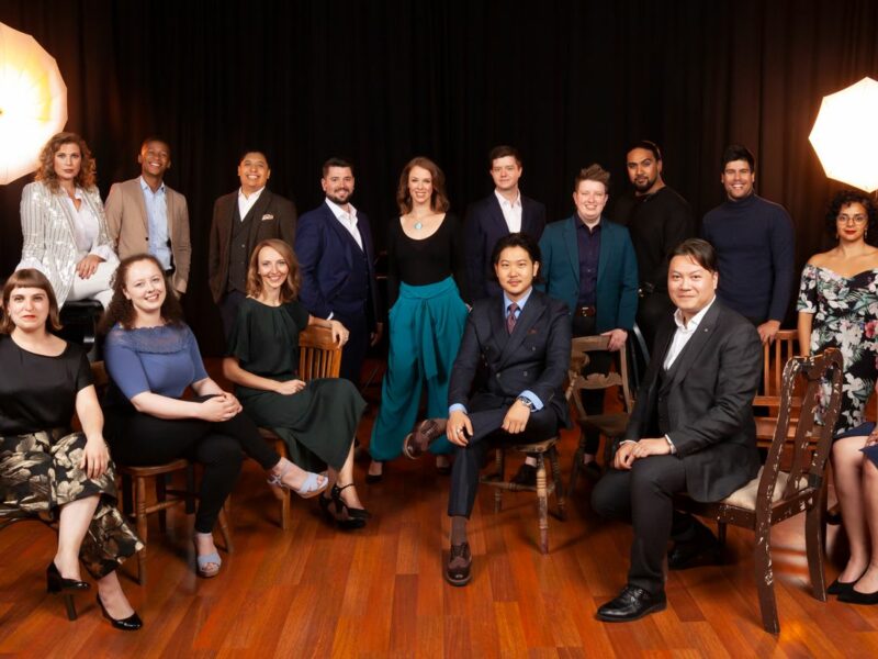 Group of young artists sat together, they are all wearing formal clothing and smiling.