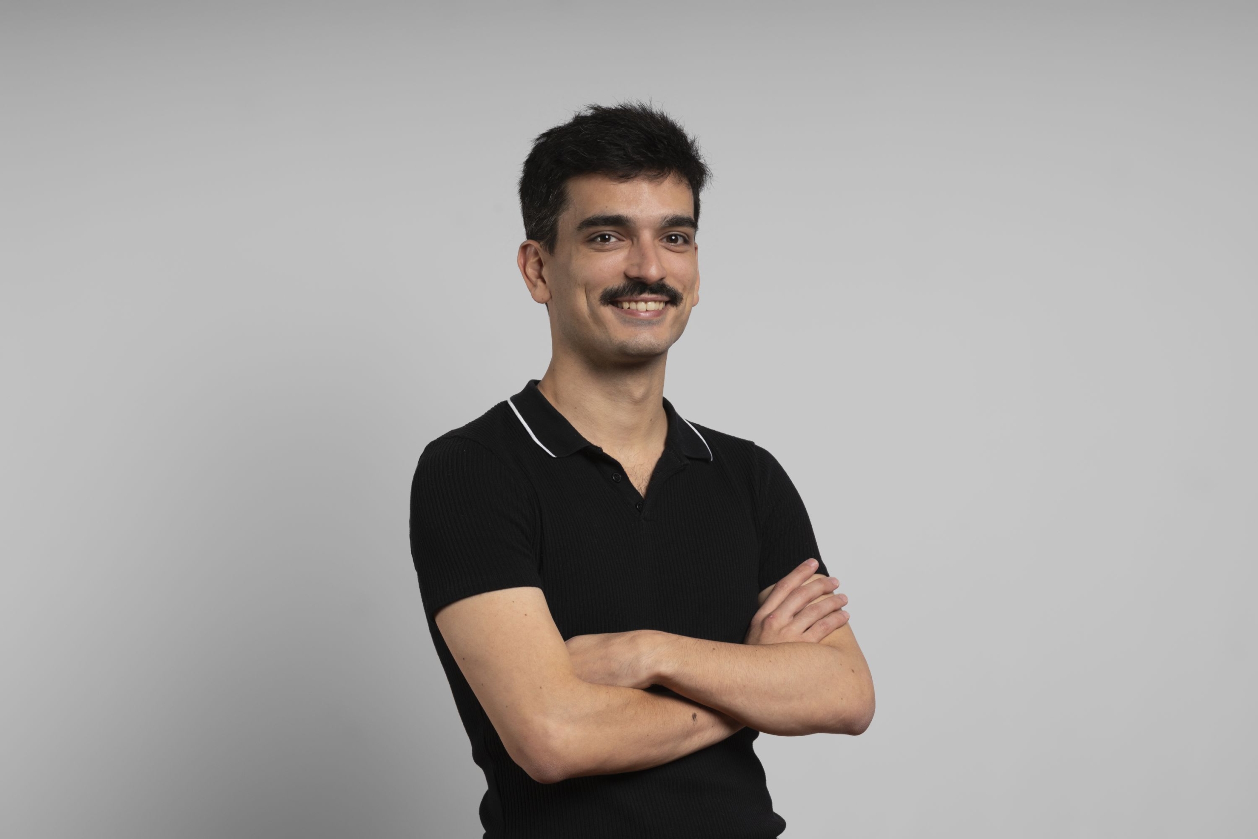 Portrait of Adrian Salinero. They have dark hair and a moustache, and are smiling at the camera.
