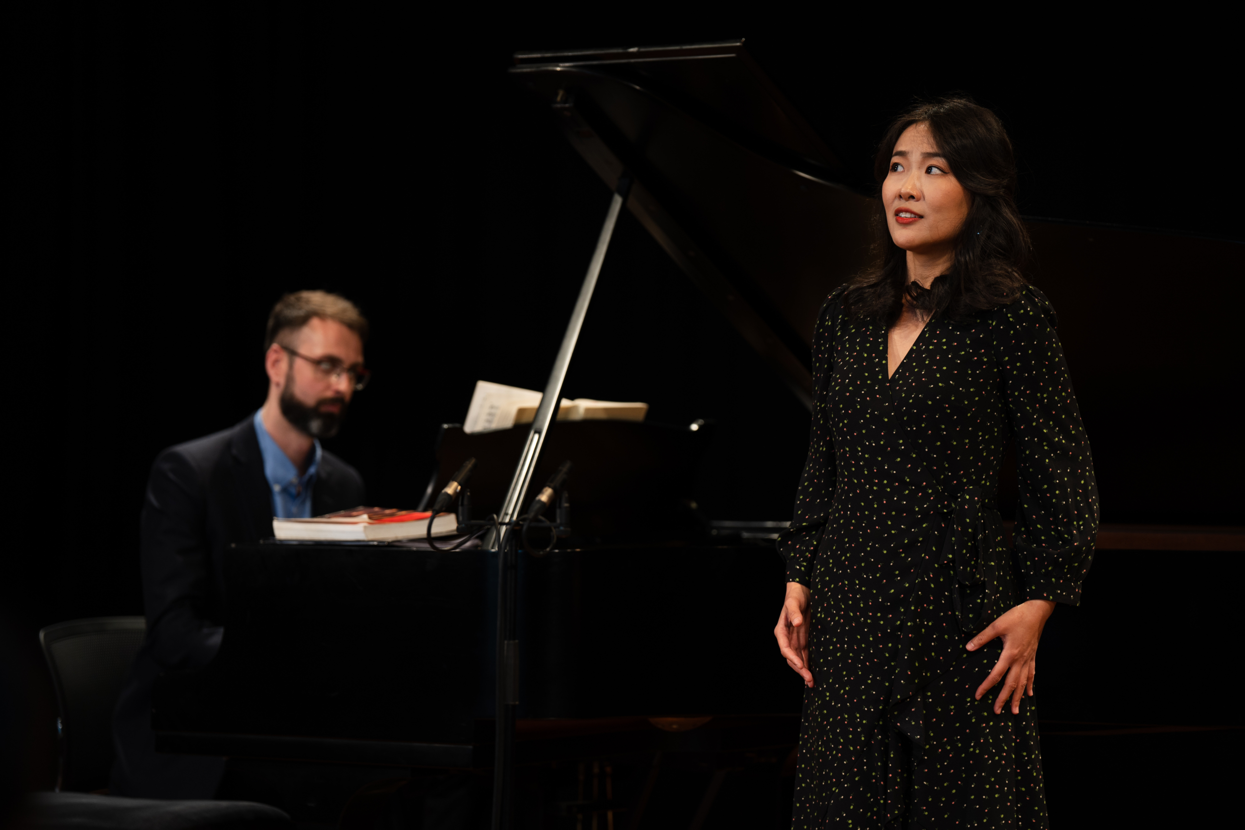 Person performing on stage with another person behind them playing piano