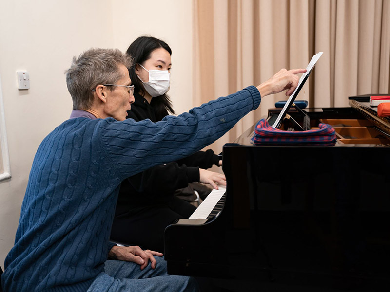 Two people sat together on the piano bench reading sheet music and performing