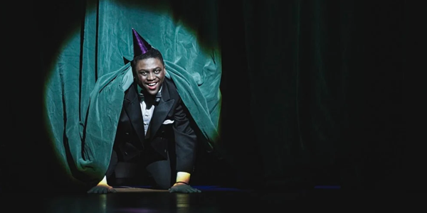 Person on all fours wearing a party hat peeking out from behind a curtain