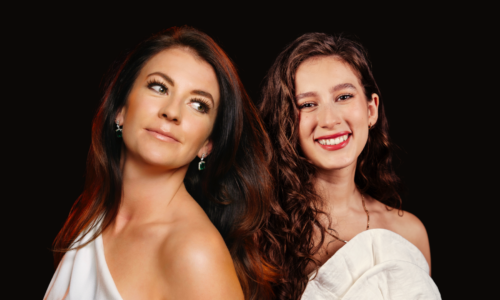 Monica McGhee and Ceferina Penny in white dresses pose in front of a black background