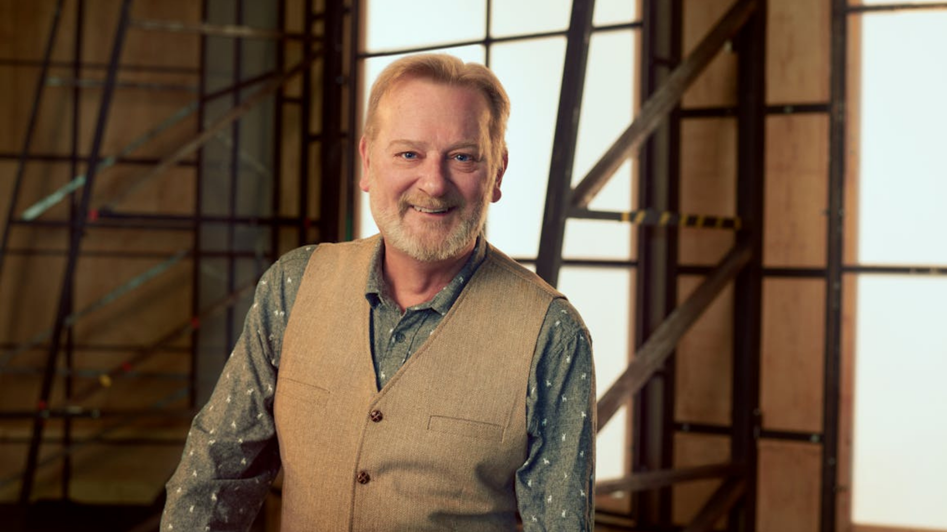 David Gowland poses smiling. He's backstage with the backs of scenery for a backdrop
